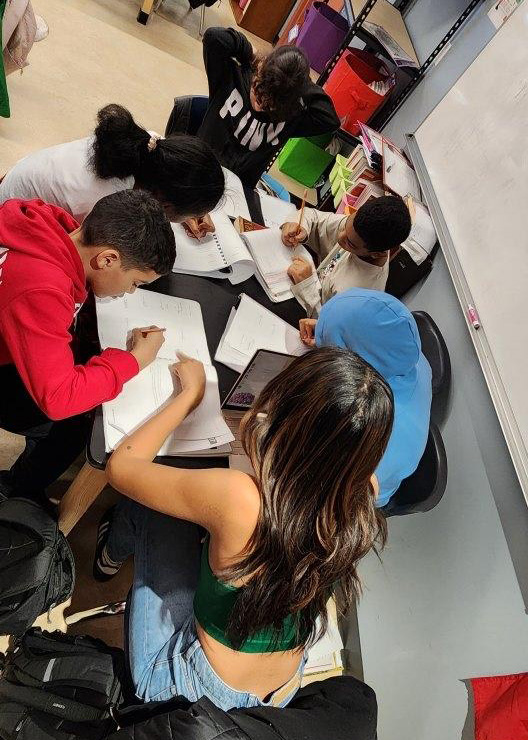 Person sitting at a table with a group of students, helping them with homework