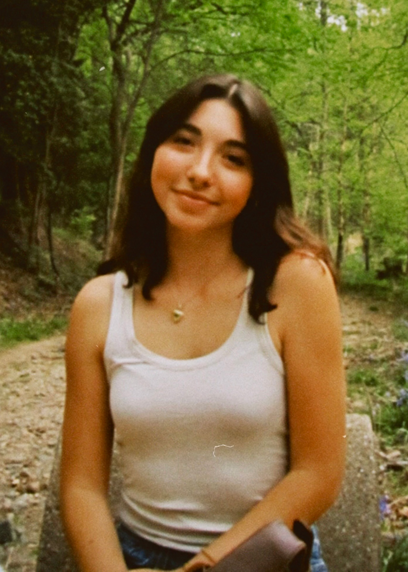 Headshot of Neena sitting in the forest wearing a white tank top
