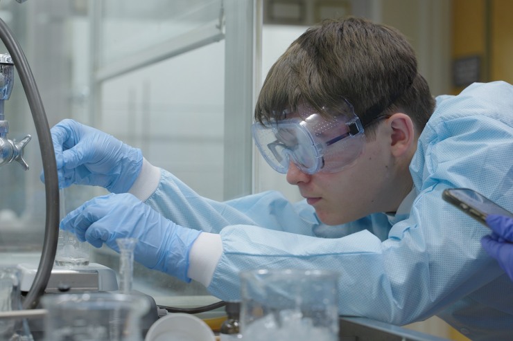 Student wearing lab gear and safety goggles conducting an experiment