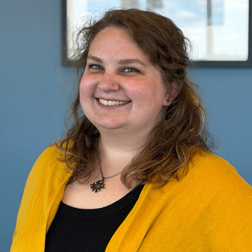 Photo of Casey Ochs standing in front of a blue wall