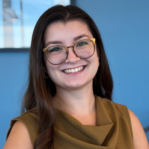 Photo of Marissa Karakny smiling at the camera, standing in front of a blue wall