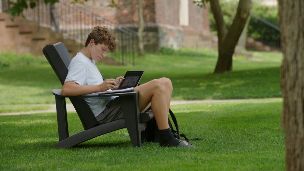 student sitting outside on a lawn chair working on his laptop