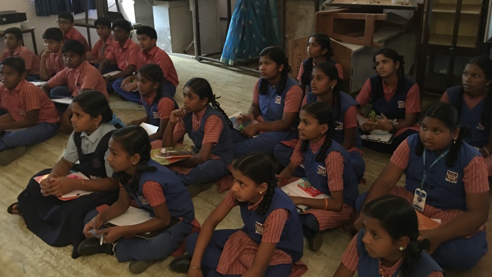 Young students sitting on a classroom floor, listening to a presentation