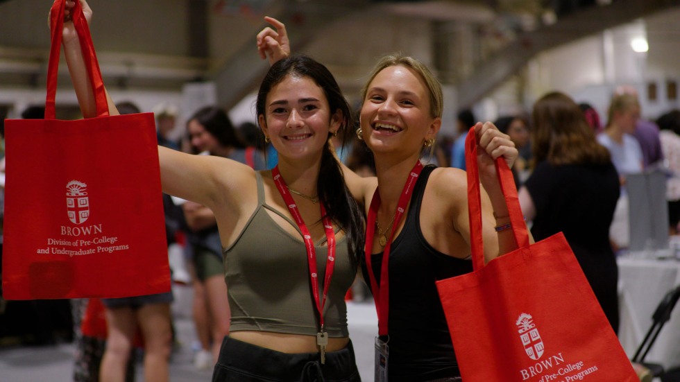 two students holding up Brown Pre-College Programs tote bags