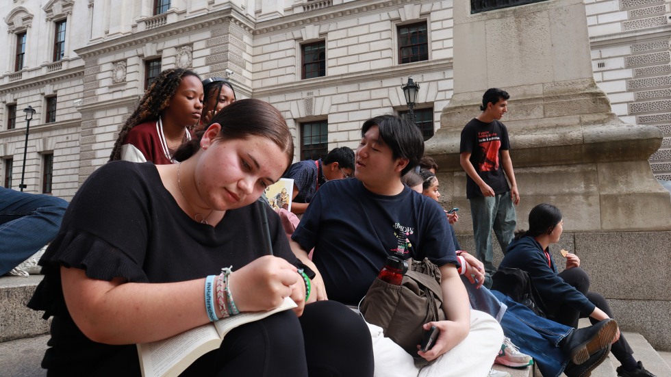 Student sitting on the steps of a building, writing in a notebook