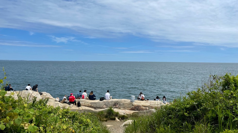 people sitting on a rock cliff overlooking the ocean